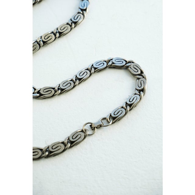 This vintage 1970s silver scroll‑link chain necklace features interlocking S‑shaped links in a woven, “snail” or...