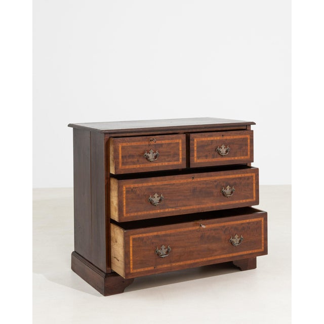 Mahogany chest of drawers in Rich Mahogany. The rich mahogany surface highlights four drawers with inlaid banding, brass...