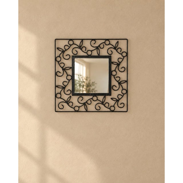 A wrought iron scroll wall mirror, small and square inside a wide frame of black iron scrollwork. Vines and curls repeat...