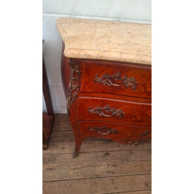 A Louis XV style marquetry commode with a marble top, resting on three drawers. The ornaments are bronze. It is curved on...