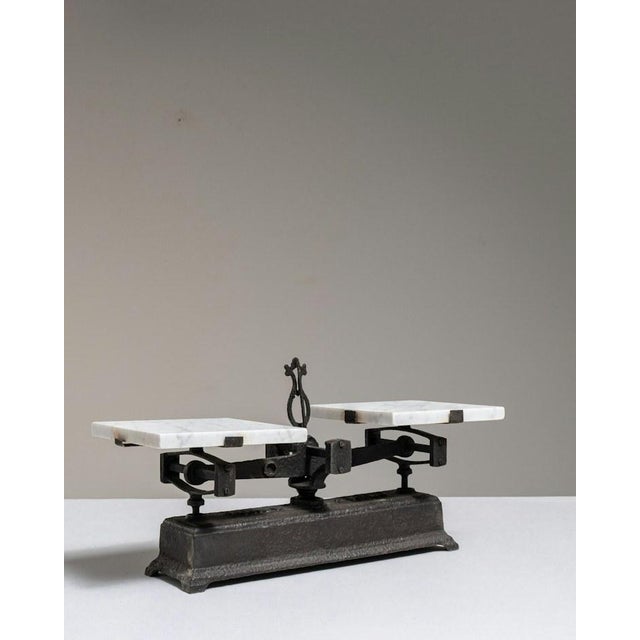 Made in France around 1900, this balance scale pairs a heavy cast iron beam and base with two pans of white marble. A...