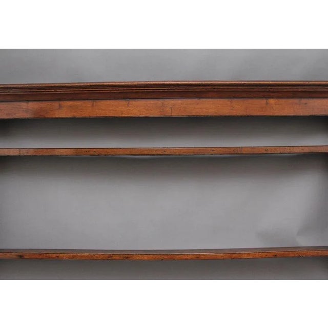 18th Century oak hanging rack, the moulded cornice above a frieze rail, two open shelves below, shaped end supports....