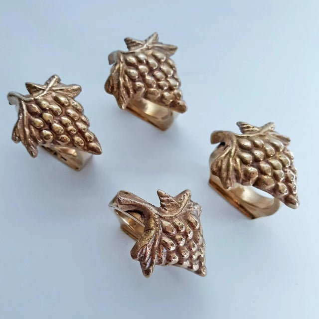 Set of 4 vintage solid brass napkin rings with vineyard motif. Each napkin ring features a cluster of grapes with leaves....
