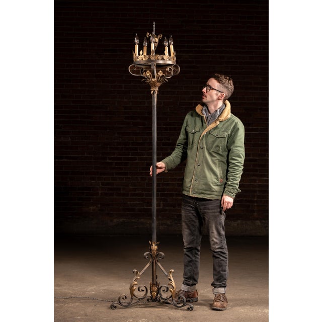 Tall wrought iron floor candelabra with a strong vertical presence, built around a slender central shaft rising from a...