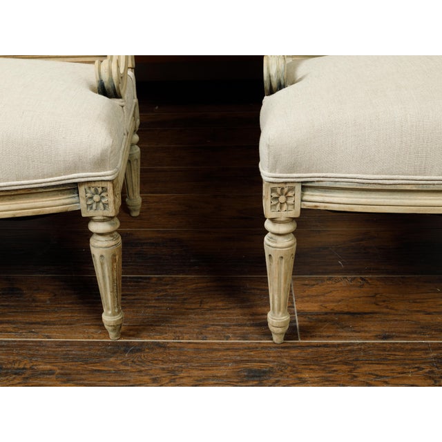 A pair of French Louis XVI style walnut settees from the early 20th century, with scrolling arm supports, fluted legs and...
