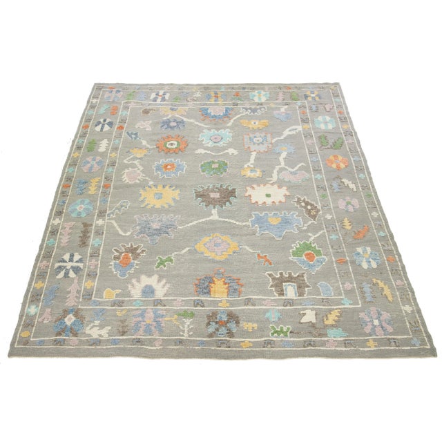 This Turkish hand-knotted wool rug showcases a light gray background adorned with a captivating multicolor floral pattern,...