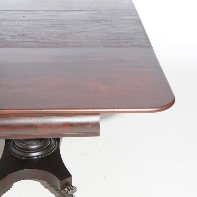 An antique American Empire Greco banquet dining table offers flame mahogany construction in Neoclassical form with drop...