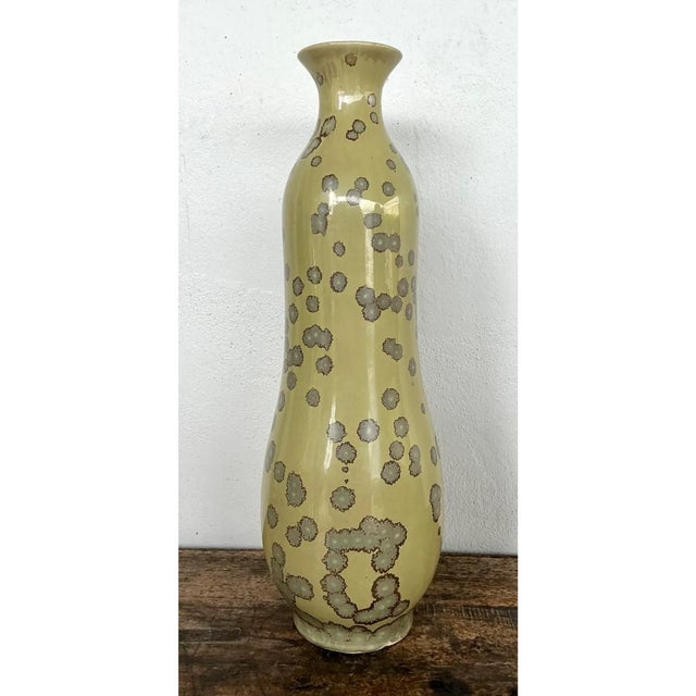 This vintage ceramic vase presents a tall, elegantly tapered gourd-like silhouette, its slender neck flaring gently to a...
