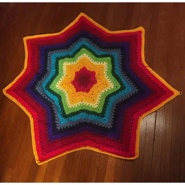 Large hand-crocheted star-shaped blanket in a full rainbow color progression, working outward from a red center through...