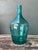 This vintage teal glass demijohn is a striking example of mid-century glassware, celebrated for its generous proportions...