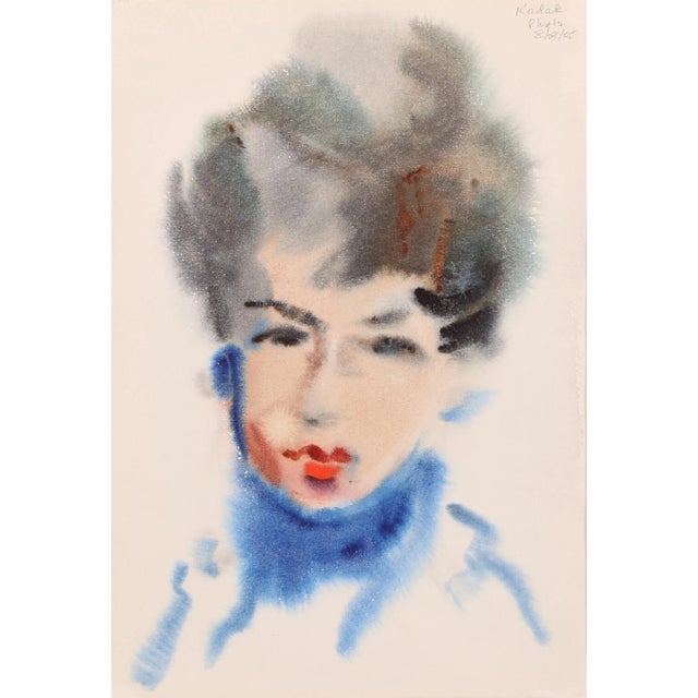 Facing the viewer, the brunette woman with red lipstick wears a royal blue turtleneck sweater that contrasts deeply with...
