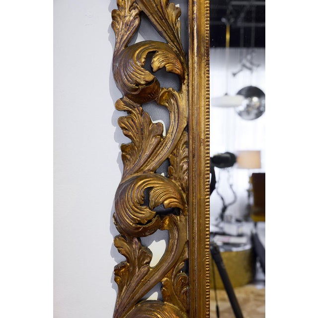 A large, carved Italian Florentine giltwood mirror featuring a bold shell and acanthus pediment and a pierced foliate...