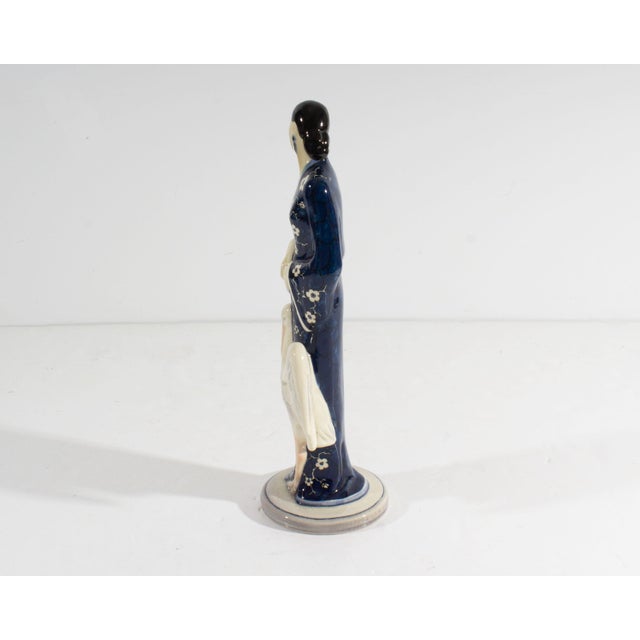 A figurine of a woman with a crane from the company Gort Bone China. A woman with black hair gazes over her shoulder,...