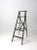 This is a vintage green wooden ladder. The painted a-frame ladder features four rung steps, a back shelf, and crossing...