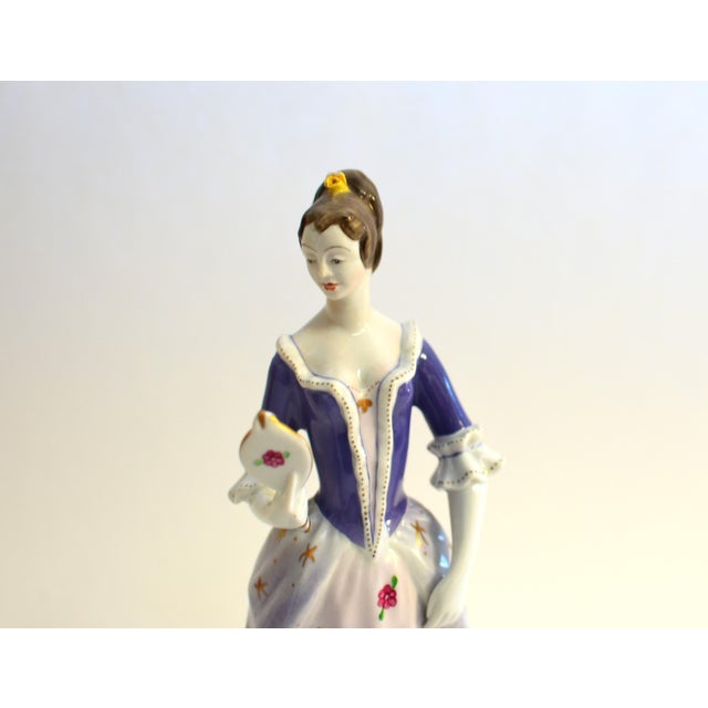 This refined Hollohaza porcelain figurine beautifully captures the grace and elegance of 18th‑century European fashion....