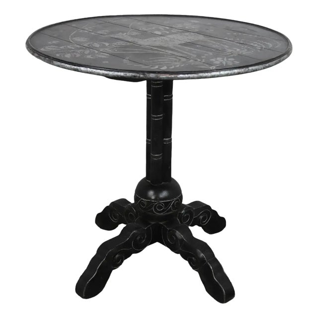 The table features a round, black lacquered tabletop adorned with delicate hand-painted plant and deer motifs, exuding a...