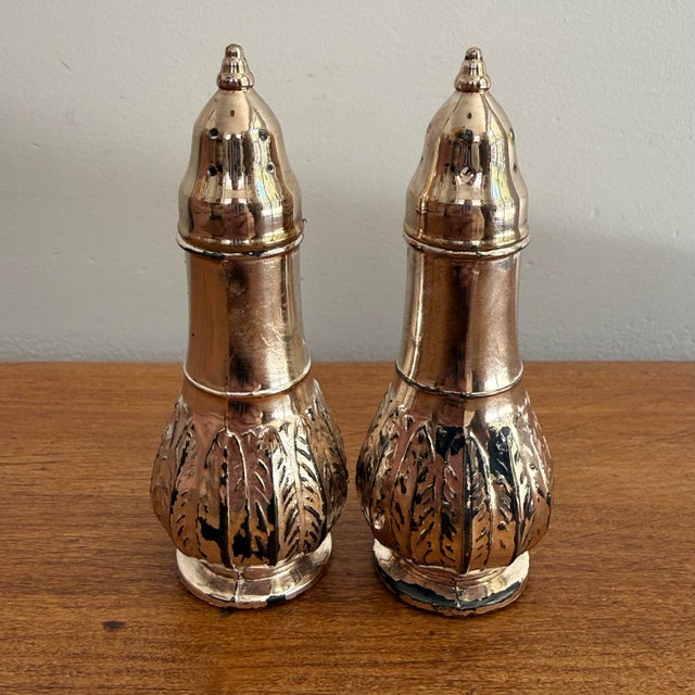 Pair of vintage silverplate salt and pepper shakers with embossed leaf bases, tapered necks, and pointed finial caps....