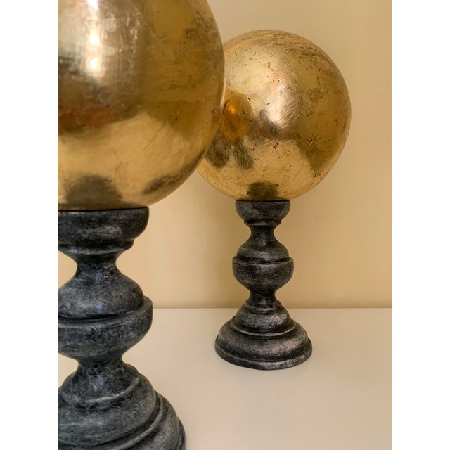 The golden wooden sphere sculpture is formed with a bright golden sphere at the top supported with a gray wooden base....
