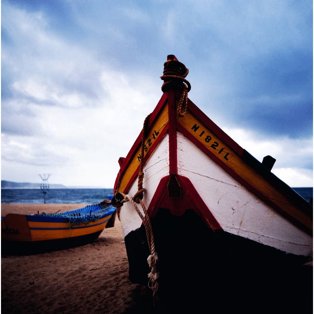 The photo shows a brightly painted fishing boat on the beach of Nazaré, a coastal town in the Centro region of Portugal....