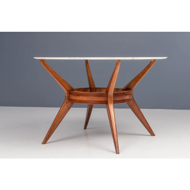 This round dining table has a remarkable wooden structure and a tabletop of white-grey marble from the Carrara region of...