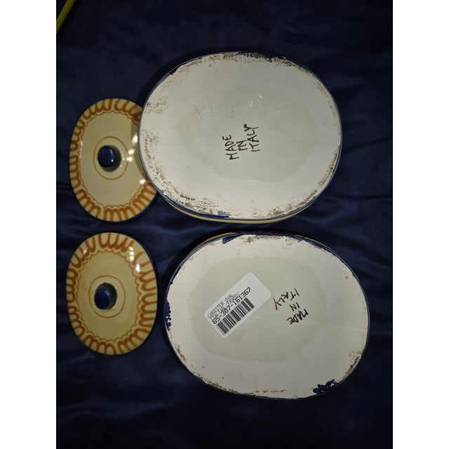 Two hand-painted Italian majolica style ceramic canisters resting on a dark blue fabric surface. Visual Details Form &...