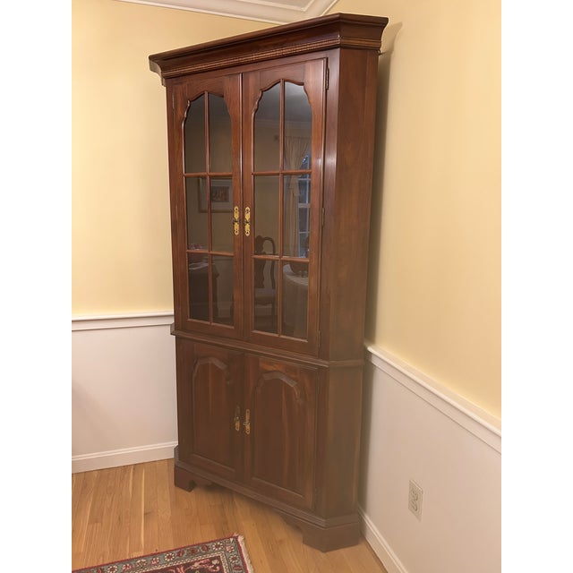 Beautiful traditional corner china cabinet crafted in rich cherry wood with elegant Colonial-inspired styling. Features a...