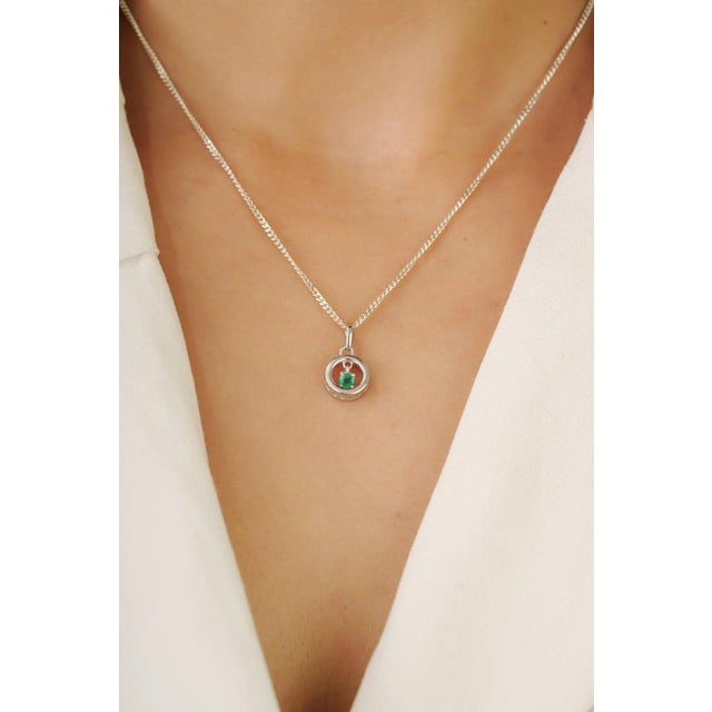 This dainty open circle pendant features a floating round emerald set in 925 sterling silver for a clean and modern look....