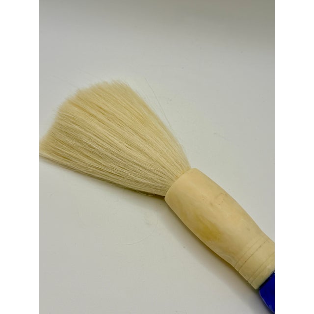 Sculptural oversized calligraphy brush featuring a richly mottled cobalt blue handle, warm ivory-tone accents, and soft...