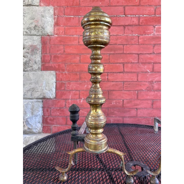 This is an impressive pair of antique brass and iron fireplace andirons featuring tall, elaborately turned baluster-form...