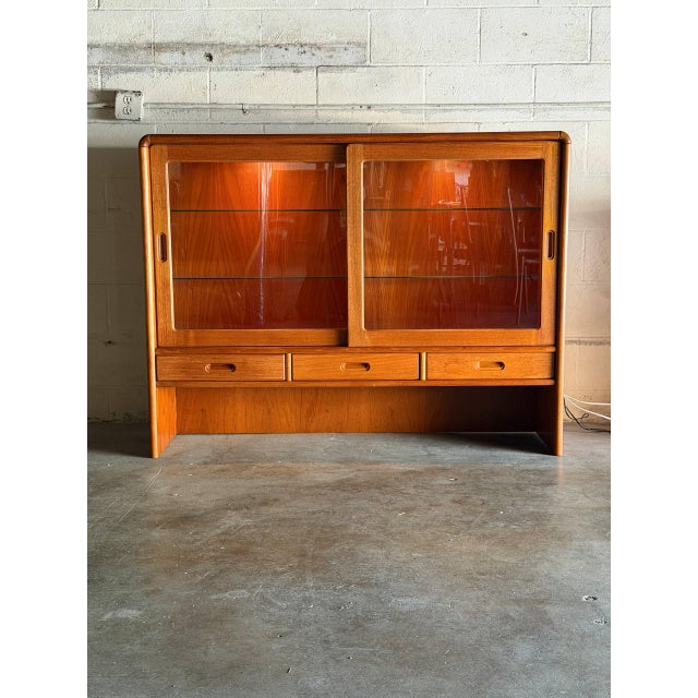 This elegant display piece showcases a minimalist silhouette with rounded top corners and sleek sliding glass doors. The...