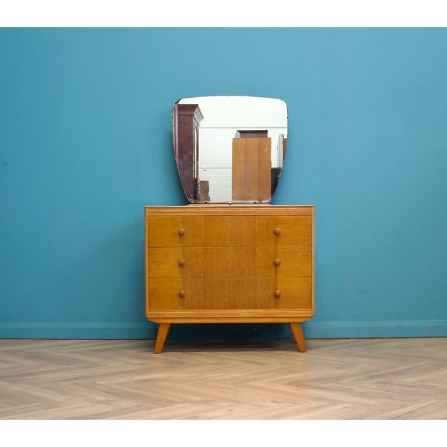 Mid-century dressing chest by Advance Furniture in light oak, standing on tapered legs. Three drawers with turned wooden...
