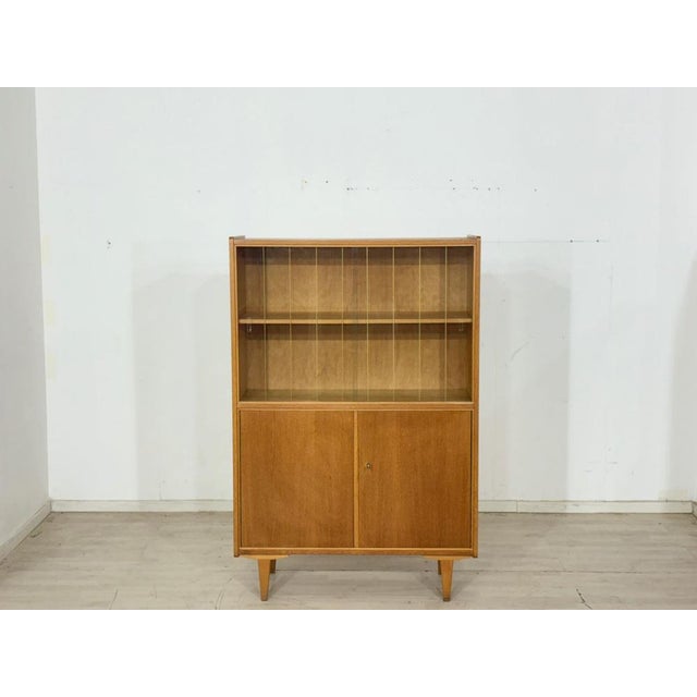 Elegant mid-century display cabinet from the 1960s. This piece of furniture impresses with its sleek design, warm wood...