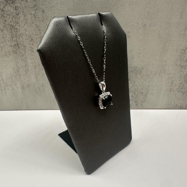 This elegant sapphire and diamond necklace in 14kt white gold features a striking cushion cut very dark sapphire totaling...