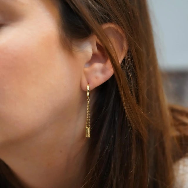 Minimalist and chic, these 14K gold huggie hoop earrings feature a dangling ball chain drop. Available in yellow or white...