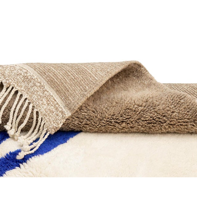 Artistic hand-knotted wool rug featuring an Ivory base with abstract Misty Taupe and Blue patterns, offering a captivating...