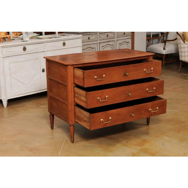 A French Louis XVI period cherry commode from the late 18th century, with three drawers and fluted side posts. Created in...