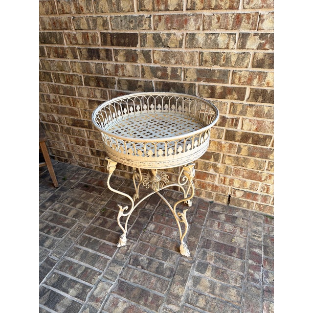 Elegant vintage wrought iron plant stand featuring a round gallery basket top with pierced leaf motif detailing and a...