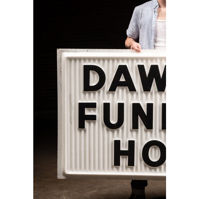 A large-scale vintage commercial sign panel displaying the words “DAWSON FUNERAL HOME” in bold, raised black lettering....