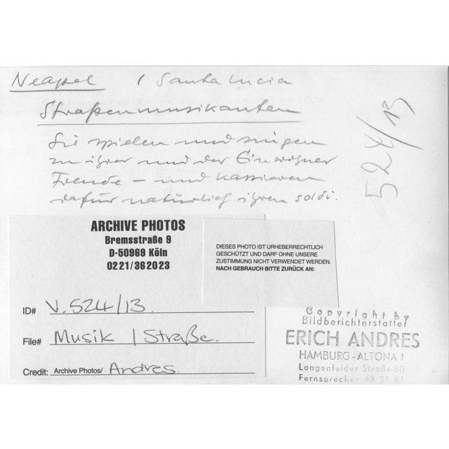 This black-and-white photograph, taken in 1952 in Naples, Italy, captures a vibrant street scene featuring musicians...