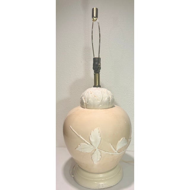 This creme and white Hollywood Regency ceramic lamp is for the dimensional band of leaves encircling its traditional...