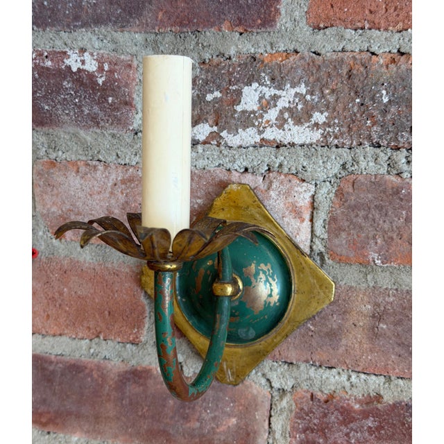 A decorative, vintage pair of toll wall sconces featuring scrolling arms painted in distressed green, with gilded foliate...