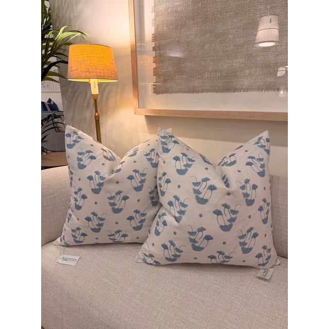 This decorative pillow features a soft white and cream background with a repeating blue leaf-inspired pattern and...