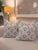 This decorative pillow features a soft white and cream background with a repeating blue leaf-inspired pattern and...