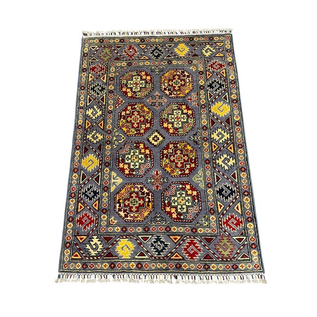 A gray field showcases eight richly colored Philpa motifs in burgundy, cream, gold, and soft green. Bold patterned borders...