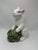 This is a glazed ceramic figurine of a white rabbit holding a cabbage. It has a soft, storybook look — the bunny is...