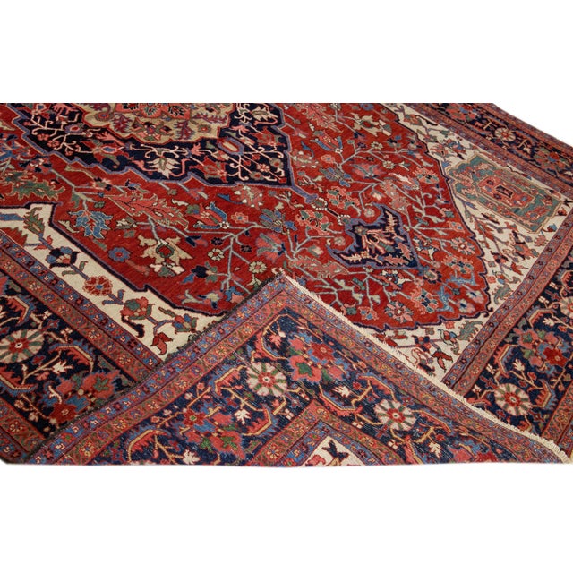 Beautiful antique Persian Heriz hand-knotted wool rug with a red field. This Heriz rug has a navy-blue frame and multi-...
