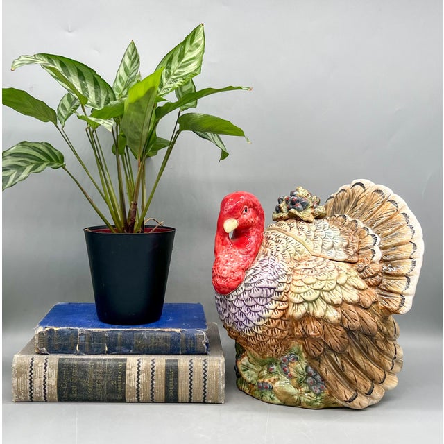 Colorful ceramic turkey cookie jar with a bright red head, layered feathers, and berries tucked among the leaves at its...