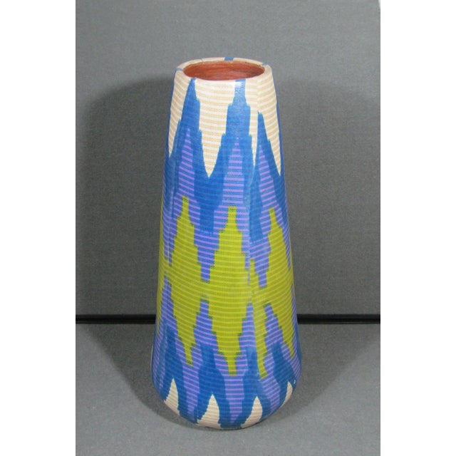 A tall, sculptural clay vase with a tapered silhouette and a bold modern geometric pattern in layered blue, purple, green,...