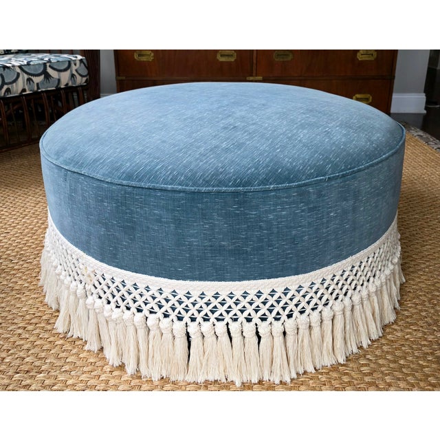 Custom upholstered ottoman in a blue cotton velvet with self welt and 8” bullion trim in off white.