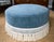 Custom upholstered ottoman in a blue cotton velvet with self welt and 8” bullion trim in off white.